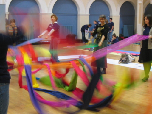 People performing a Giant Weave indoors and weaving fabric as they move